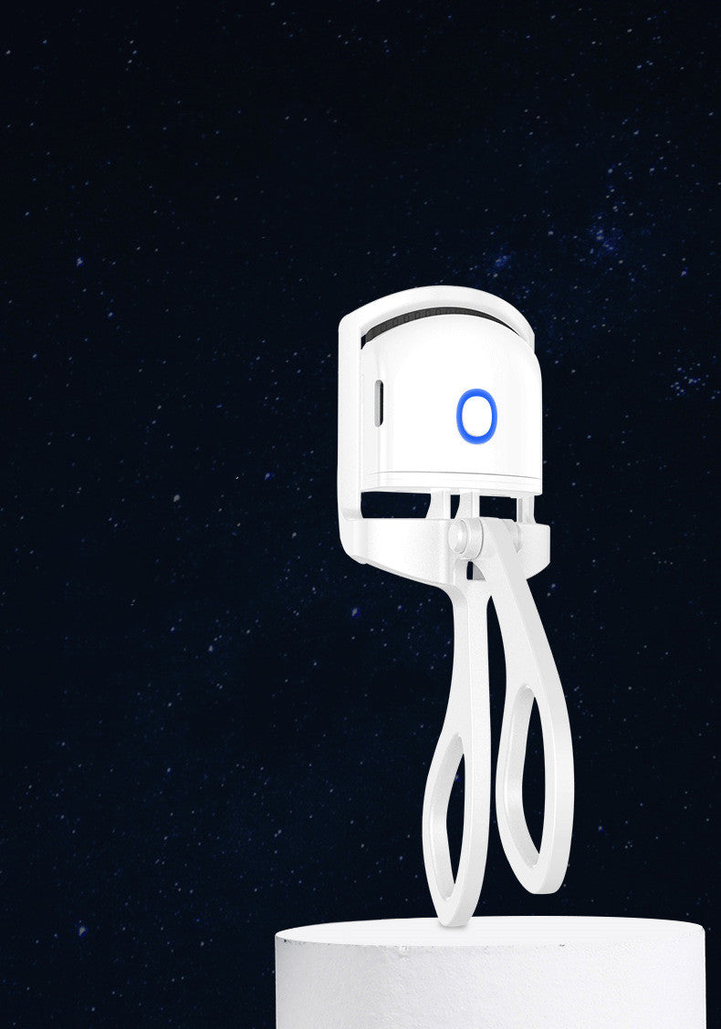 White heated eyelash curler with blue circle light, mounted on a stand against starry background.